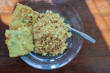 Kahvaltı tabağının fotoğrafı masanın üstünde. Yanında da yumurta pilavı ve 2 kızarmış tempeh ve cam bir tabakta servis ediliyor.
