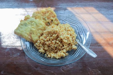 Kahvaltı tabağının fotoğrafı masanın üstünde. Yanında da yumurta pilavı ve 2 kızarmış tempeh ve cam bir tabakta servis ediliyor.