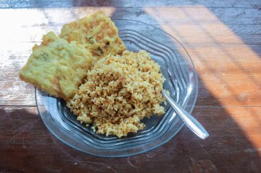 Kahvaltı tabağının fotoğrafı masanın üstünde. Yanında da yumurta pilavı ve 2 kızarmış tempeh ve cam bir tabakta servis ediliyor.