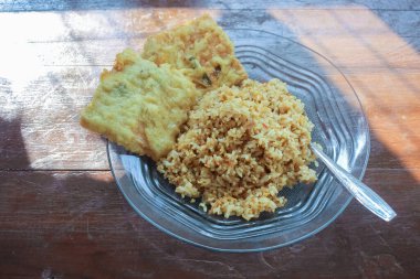 Kahvaltı tabağının fotoğrafı masanın üstünde. Yanında da yumurta pilavı ve 2 kızarmış tempeh ve cam bir tabakta servis ediliyor.