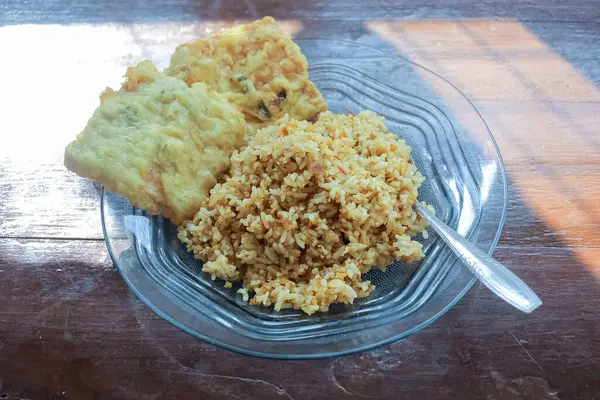 Kahvaltı tabağının fotoğrafı masanın üstünde. Yanında da yumurta pilavı ve 2 kızarmış tempeh ve cam bir tabakta servis ediliyor.