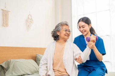 Asyalı kadın fizyoterapist, yatak odasında yaşlı kadın hastaya ağırlık kaldırmayı öğretiyor. Yaşlılar Sağlık ve Sağlık Hizmetleri, Fizik Terapi ve Bakım Evi.