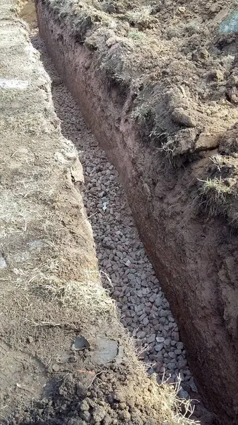 Kanalizasyon boruları döşemek için arazide siper kazmak. Binalar