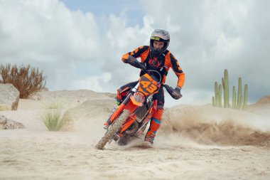 Genç adam toprak motosiklet sürme alıştırması yapıyor. Kum sıçrıyor