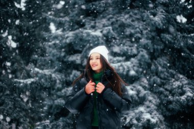 Beyaz kış şapkalı esmer kadın, karlı parkta yürüyor. 