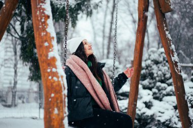Beyaz kış şapkalı esmer kadın, karlı parkta yürüyor. 