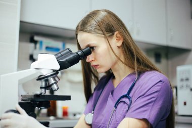 Kadın mikroskopla bir şeye bakıyor.