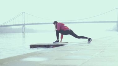 Şehirde nehir kıyısında gerinen sportif kız
