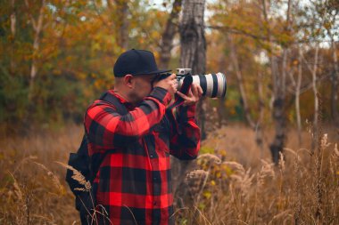 Orman arka planında kamera olan bir fotoğrafçı.