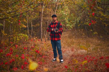 Genç bir adam elinde sırt çantasıyla ormanda yürüyor. Sonbaharda kırmızı ceketli ve kot pantolonlu bir adam.