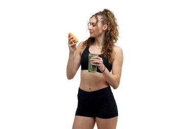 Spor kıyafetli genç bir kadın bir dilim portakal ve bir şişe meyve suyuyla hamburger yiyor. beyaz arkaplanda izole.