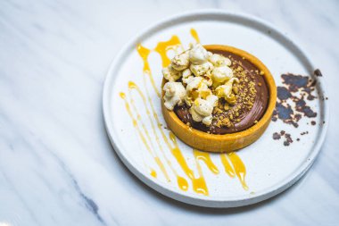 Bisküvi bazlı çikolatalı tart, çikolata ganache, patlamış mısır ve karamel sosu.