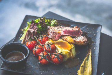 NZ pirzola bifteği, tavada az pişmiş, yanında gerçek köy kremalı patates püresi, sarmaşıklı vişneli domates, salata.