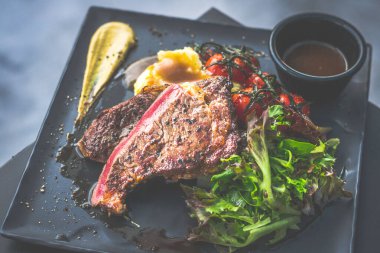 NZ pirzola bifteği, tavada az pişmiş, yanında gerçek köy kremalı patates püresi, sarmaşıklı vişneli domates, salata.