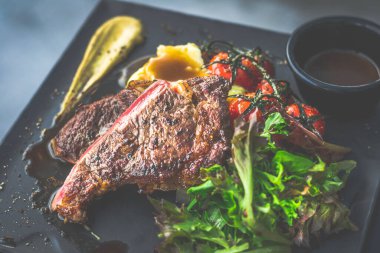 NZ pirzola bifteği, tavada az pişmiş, yanında gerçek köy kremalı patates püresi, sarmaşıklı vişneli domates, salata.