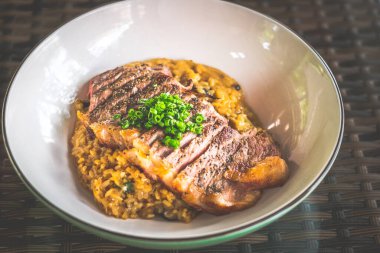 Risotto served with angus medium rare ribeye steak in a bowl clipart