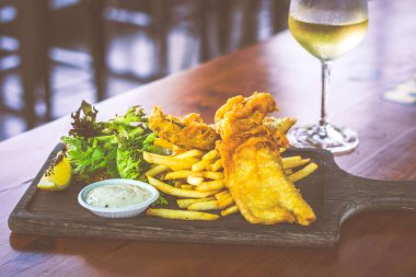 Bira ezilmiş balık ve patates kızartması, salata ve tartar sosuyla ahşap tabakta servis edilir.