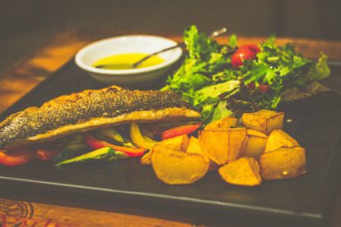 Gri İtalyan deniz ürünleri sotelenmiş sebze ve kızarmış patatesle servis edilir.