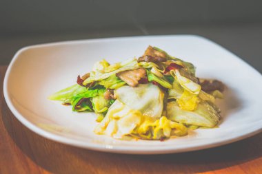 Lahanayla kızartılmış lahana, domuz göbeği, beyaz tabakta servis edilen kurutulmuş kırmızı biber.