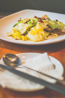 Lahanayla kızartılmış lahana, domuz göbeği, beyaz tabakta servis edilen kurutulmuş kırmızı biber.