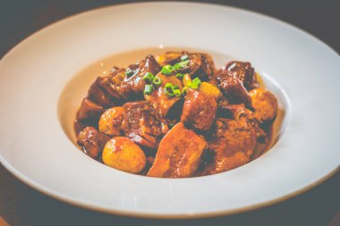 Pirinçli domuz eti, kızarmış bıldırcın yumurtası ve taze soğan süslemesi beyaz bir tabakta servis edilir.