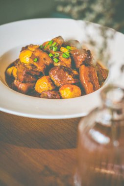 Pirinçli domuz eti, kızarmış bıldırcın yumurtası ve taze soğan süslemesi beyaz bir tabakta servis edilir.