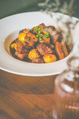 Pirinçli domuz eti, kızarmış bıldırcın yumurtası ve taze soğan süslemesi beyaz bir tabakta servis edilir.