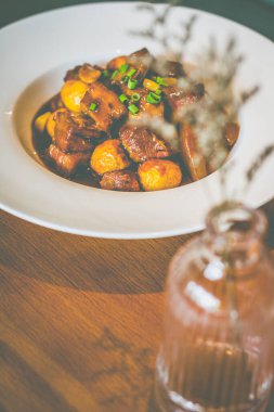 Pirinçli domuz eti, kızarmış bıldırcın yumurtası ve taze soğan süslemesi beyaz bir tabakta servis edilir.