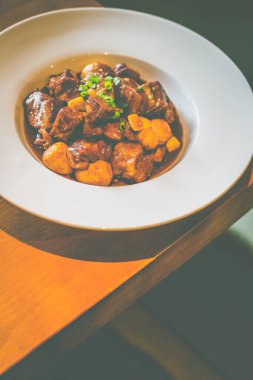 Pirinçli domuz eti, kızarmış bıldırcın yumurtası ve taze soğan süslemesi beyaz bir tabakta servis edilir.