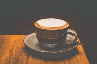 Kahverengi bir fincanın üstünde beyaz süt köpüğü olan bir bardak kapuçino.