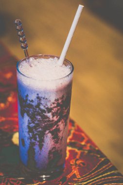 Bir bardakta böğürtlen aryanı ve masada pipet.