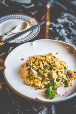 Beyaz bir tabakta kokulu konserve turpla servis edilmiş ipek gibi düz pirinç erişteleri.