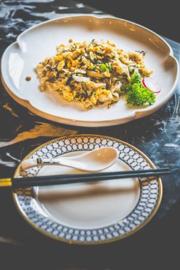 Beyaz bir tabakta kokulu konserve turpla servis edilmiş ipek gibi düz pirinç erişteleri.