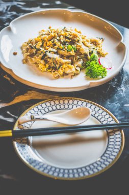 Beyaz bir tabakta kokulu konserve turpla servis edilmiş ipek gibi düz pirinç erişteleri.