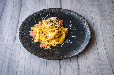 Jambon kremalı ve peynirli, siyah tabakta servis edilen Carbonara.