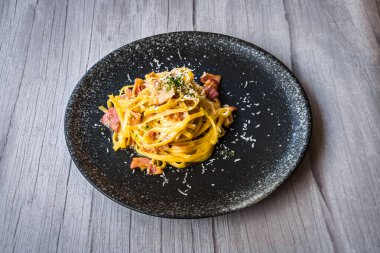 Jambon kremalı ve peynirli, siyah tabakta servis edilen Carbonara.