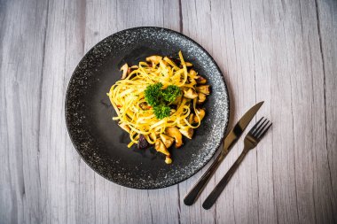 Mantar Aglio Olio makarnası masada siyah bir tabakta servis edilir.