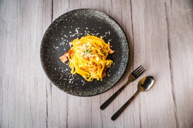 Jambon kremalı ve peynirli, siyah tabakta servis edilen Carbonara.
