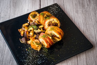 Siyah tabakta servis edilen sotelenmiş mantarlı tavuk roulade.