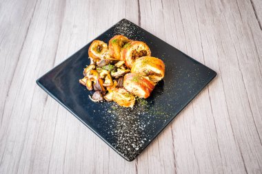 Siyah tabakta servis edilen sotelenmiş mantarlı tavuk roulade.