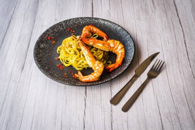 Kaplan karidesli Chimichuri Makarnası siyah bir tabakta servis ediliyor.