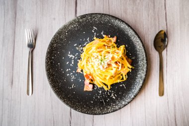 Jambon kremalı ve peynirli, siyah tabakta servis edilen Carbonara.