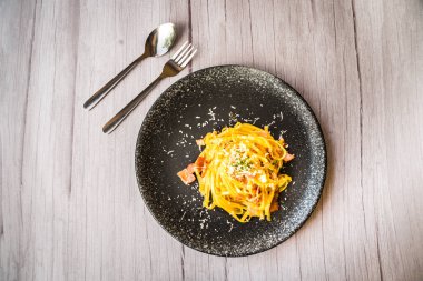 Jambon kremalı ve peynirli, siyah tabakta servis edilen Carbonara.