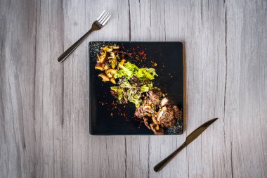 Siyah tabakta servis edilen salata ve sotelenmiş mantarlı biftek küpü.