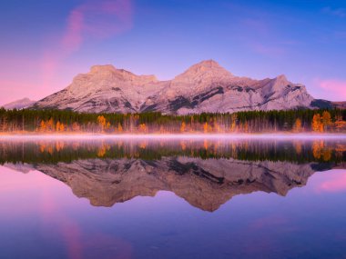 Şafak vakti dağ manzarası. Sisli bir sabah. Şafakta bir dağ vadisinde göl ve orman. Parlak güneş ışığıyla doğal manzara. Gölün yüzeyindeki yansımalar. Banff Ulusal Parkı, Alberta, Kanada. 