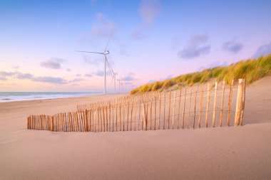 Gün batımında deniz kıyısında sörf. Yenilenebilir enerji kaynakları. Kıyıda rüzgar türbinleri. Hollanda 'da. Gün batımında deniz manzarası. Gün batımında parlak gökyüzü. Dalgalar alçaldığında kumlu bir sahil. Endüstriyel görüntü. 