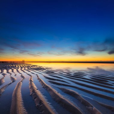 Gün batımında deniz manzarası. Deniz kıyısındaki kum hatları. Gün batımında parlak gökyüzü. Dalgalar alçaldığında kumlu bir sahil. Seyahat görüntüsü. Tasarım fotoğrafçılığı.