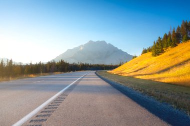 View of the road during sunset. High mountains on the horizon. Bright sun during sunset. Direction of movement. Wallpaper and background. Nature. Transport theme.