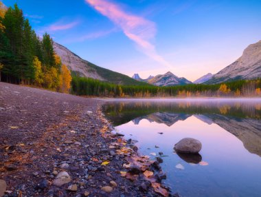 Lake and mountains in a valley at dawn. Reflections on the surface of the lake. Mountain landscape at sunrise. Foggy morning. Natural landscape with bright sunshine.