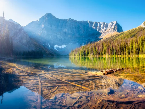 Rawson lake, Canada. Lake and mountains in a valley. Reflections on the surface of the lake. Mountain landscape at sunrise. Foggy morning. Natural landscape with bright sunshine.
